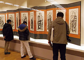 福光美術館で棟方志功の「二菩薩釈迦十大弟子」の屏風に見入る来館者＝いずれも富山県南砺市で