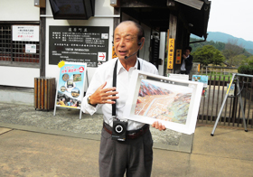 遺跡の復原図を手に観光客に話しかける岸田清さん