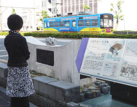 与謝野晶子の生家跡にある晶子自筆の刻字の歌碑。その上には晶子の好んだユリとアマリリスの彫刻。向こうを阪堺電車が通る