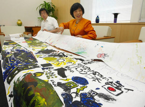 世界の子どもたちが描いた東北激励の絵を見せる近藤さん（右）ら＝中日新聞北陸本社で