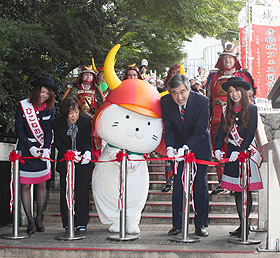 彦根城フェス開幕を祝いテープカットするひこにゃん（中央）と参加者たち＝彦根市金亀町の開国記念館で