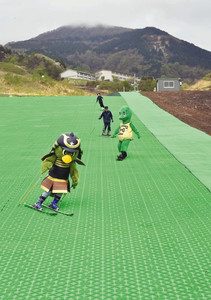 緑色のマットで作られた人工ゲレンデの滑り心地を確認するマスコットら＝大野市の六呂師高原スキーパークで