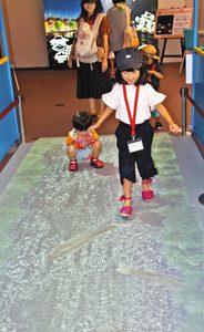床に映し出された矢勝川の魚を追い掛けて遊ぶ子どもたち＝半田市中村町のミツカンミュージアムで