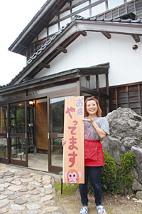 民家を改装して開店した「ごはん家ござる」。開店の看板を掲げる渡辺有美子さん＝宝達志水町森本で