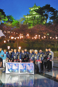 城を背景にぼんぼりに点灯する関係者たち＝坂井市の丸岡城で