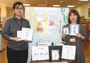 オノマトペだけで紹介された本を手にする吉田さん（左）ら＝瑞浪市土岐町の瑞浪市民図書館で