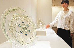 塚原梢さん（右）が繊細な装飾を施したガラスの皿などが並ぶ作品展＝金沢市武蔵町で
