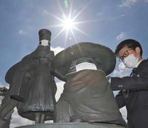市職員からマスクを着けられる、銀河鉄道９９９のメーテル（左）と鉄郎のブロンズ像＝伊賀市で