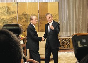 北京の釣魚台迎賓館で、福田康夫元首相と握手しながら報道陣に撮影を促す王毅外相（右）