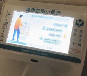 公衆トイレの便器に装着された画面。安全性やプライバシー保護を強調し、尿検査を促す内容