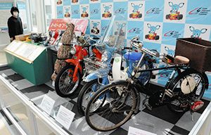 スーパーカブをテーマにした特別展。シリーズの原点ともいえる自転車用の補助エンジン（手前）も並ぶ＝鈴鹿市役所で