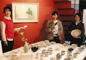 安藤さんが製作した食器の前に並ぶ左から近藤さん、中神さん、小崎さん＝瑞浪市稲津町の瑞浪芸術館で