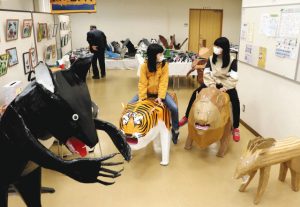 ライオンやトラを模した段ボールアートに乗って遊ぶ子どもたち＝松本市島内公民館で