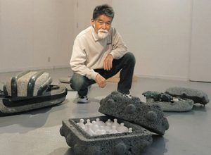 石の入れ物に入った立体作品を紹介する水野さん＝池田町草深の極小美術館で
