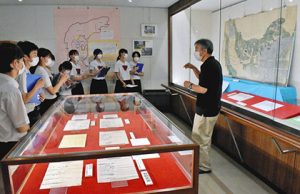 長連龍に関連する書状などが並ぶ会場で、生徒たちを案内する岡本伊佐夫さん（右）＝穴水町川島の町歴史民俗資料館で
