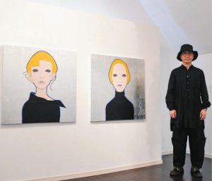 顔をテーマにした作品と北村さん＝いずれも池田町草深の極小美術館で