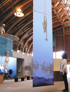 重りを手に潜る海女のシルエットを映し出すタペストリー。奥はフナド海女漁の模型＝鳥羽市海の博物館で